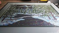 Framed Lovett print showing a stylized Canadian winter scene with snow, trees, and a stream, signed Lovett.