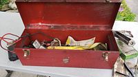 Red metal toolbox open on table showing various hand tools inside and some outside beside it.