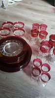 Overview photo of 25-piece Mid Century Modern glassware with clear glass bodies and red rims, including plates, bowls, and various glasses.