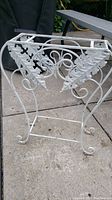 Front-side view of the white painted iron stand showing decorative scrollwork and leaf-shaped elements on the sides.