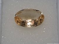 Close-up photo of oval cut citrine gemstone showing faceted surface and light golden yellow color.