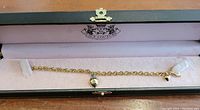 Juicy Couture gold-tone charm bracelet inside the original pink-lined black box, showing two charms attached.