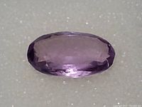 Close-up photo of a light purple oval cut amethyst gemstone on white textured surface