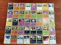 Flat lay photo showing all 40 Pokemon cards arranged in a grid on a wooden floor, showcasing the front artwork and text of each card.