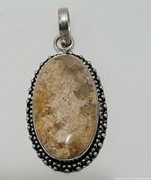 Front view of oval sterling silver pendant featuring a large stone with beige and cream patterns, detailed with a beaded border.