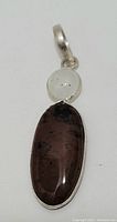Front view of sterling silver pendant with oval dark brown stone and round moonstone above it, showing overall design and color.