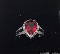 Front view of the sterling silver ring featuring a pear-shaped red gemstone surrounded by small clear accent stones.