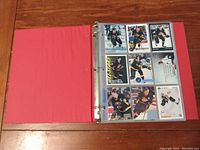 Red 3-ring binder open to show clear plastic sleeves containing hockey cards of Vancouver Canucks players, mainly black uniformed, from the 1990s.