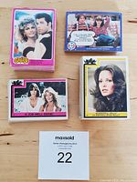 Four stacks of 1970's trading cards, including characters and scenes from Grease, Charlie's Angels, and Mork & Mindy. Cards show photographic scenes and portraits.