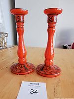 Pair of orange Tango glass candle holders with black floral design and silver overlay on wooden table with lot number card.