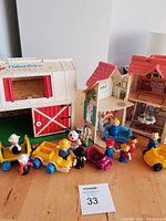 Photo showing vintage Fisher-Price barn, house, multiple figures, and vehicles arranged on wooden surface.