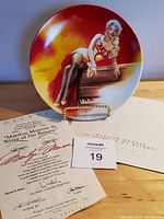 Collector plate of Marilyn Monroe in a red dress reclining on a log photographed with Certificate of Authenticity and original envelope on wooden surface.