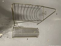 Vintage brass metal record holder rack with curved wire slots, decorative detail at one end, placed on floor.