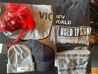 Overview photo showing t-shirts, hats, a baseball cap, a red tote bag, and some folded items in grey and black with Nine Inch Nails logos and text.