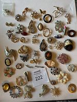Top-down view of about 40 vintage brooches with diverse styles including floral, butterfly, face cameo, abstract, animal shapes, and bow motifs made from mixed metals with rhinestones and enamel accents.