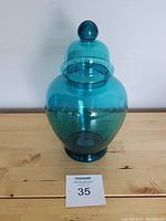 Front view of vintage turquoise glass candy jar with lid on wooden surface.