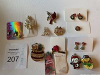Photo shows a spread of various vintage Christmas-themed jewellery pieces including pins shaped like a cardinal, wreaths, and Christmas trees, along with small festive stud earrings and penguin charms on a Claire's branded card.