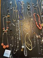 Photo showing wide assortment of costume necklaces laid out on dark surface, featuring variety of materials and colors.