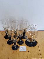 Six vintage champagne flute/pilsner glasses arranged in two rows and one vintage hurricane lamp on the right side with clear glass globes and black bases.