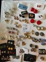 Full lot of various vintage clip-on and screw-back costume earrings arranged on white surface.