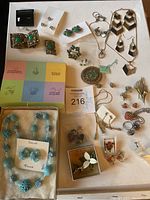 Overview of multiple vintage fashion jewelry pieces arranged on a flat surface including earrings, rings, brooches, pendants, and a boxed blue bead necklace set.