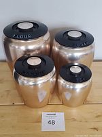 Full set of four copper aluminum canisters labeled flour, sugar, coffee, and tea with black lids and cream knobs.
