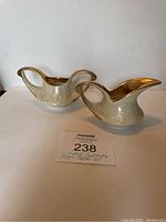 Two vintage ceramic creamers with gold-toned handles and spouts, iridescent pearly white finish with decorative embossing.