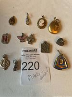 Eleven assorted vintage pendants displayed on a white background, showing variety of shapes and designs including a cameo, butterfly, figures, and geometric shapes.