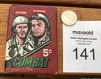 Front view of sealed 1964 Donruss Combat wax pack with illustrated soldiers and 5 cents price, placed beside a quarter for size reference, along with auction lot number.