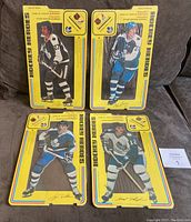 Four Hockey Heroes laminated stand-ups in original packaging shown upright on a couch, featuring Darryl Sittler, Borje Salming, Tiger Williams, and Erroll Thompson.