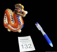 Full side view of the colorful dragon figurine on black background with pen for scale and auction number 132