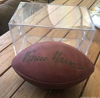 Wilson NFL football autographed by Franco Harris in gold Sharpie, positioned in front of the Lucite display case.
