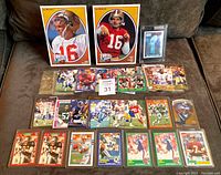 Overview of 50 NFL football cards laid out on a brown surface including 2 oversized Joe Montana Upper Deck Football Heroes cards and many others.