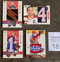 Lot of four Montreal Canadiens jersey and patch cards featuring players Jean Beliveau, Jacques Plante, Georges Vezina, Vladislav Tretiak, laid out on dark surface.