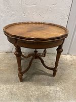 Front angled view of antique wooden side table showing scalloped edge top, legs, and base structure.