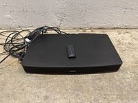 Black Bose Solo TV Sound System placed on the ground with cables and remote on top.