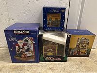 Four boxed Christmas ceramic collectible items including Kirkland fabric Santa, Dickensville Firehall, Twin Sleepy miniature, and an additional ceramic house with lit windows