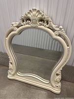 Front view of the decorative mirror showcasing the full ornate cream frame and reflective surface