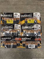 Top-down photo showing six packs of Duracell AA CopperTop batteries arranged on a concrete floor including four packs of 20 batteries and two packs of 16 batteries.