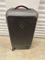 Front view of black Herschel hard shell suitcase with ridges and diamond-shaped logo.