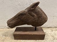 Front left angle of hand-carved wooden horse head mounted on wooden base, showing detailed carving of mane and ear.