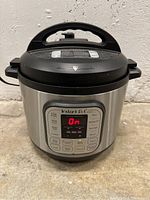 Full view of the Instant Pot IP-DUO showing the stainless steel body and black lid with handle.