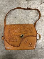 Full front view of the tan leather purse showing embossed rose design and JB initials on flap with braided trim and brass twist lock.