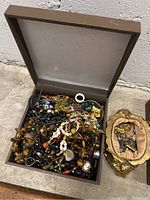 Box filled with assorted jewelry including beaded necklaces, metal chains, rings, brooches