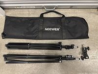 Two black Neewer light stands folded with adjustment clamps and mounting screws next to a black Neewer branded carrying bag with handle.