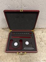 Open wooden case containing putter components, golf balls, and ball marker.