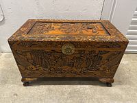 Front view of chest showing lid, front panel carvings, metal clasp lock and carved feet