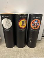 Three black cylindrical tubes upright side by side each with colorful circular artistic labels featuring abstract figures and faces. Tubes read Ritzenhoff and include numbers 22648, 22450, 22649.