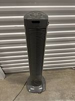 Full view of gray Seville Classics tower fan standing on concrete floor with cord visible.