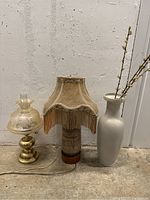Full view of two vintage table lamps on a concrete floor next to a tall white ceramic vase with faux pussy willow branches.